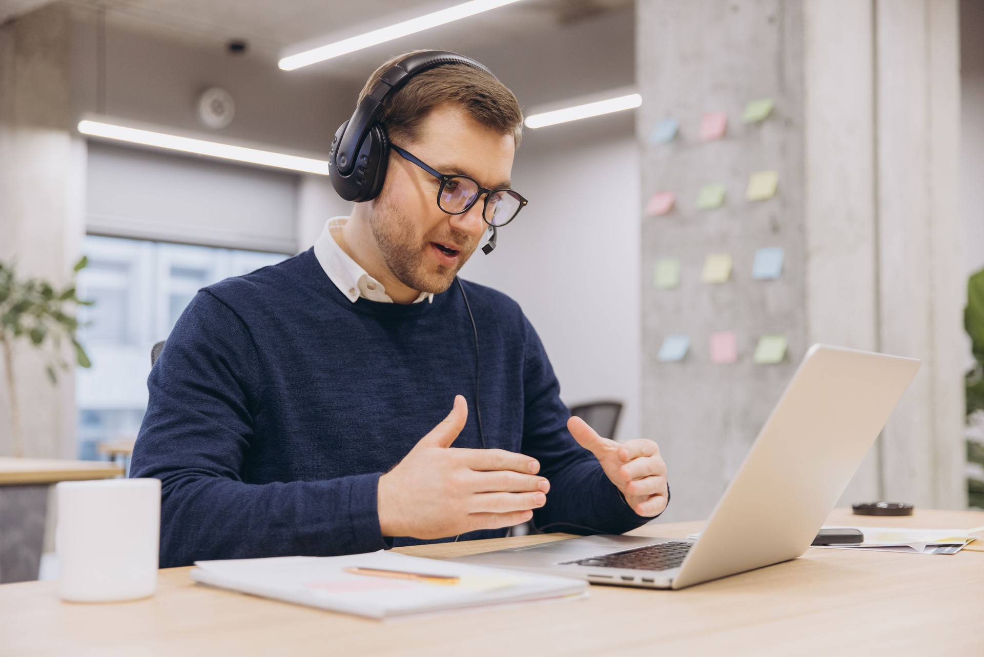 Businessman wearing headset is speaking and gesturing during video call on laptop in office